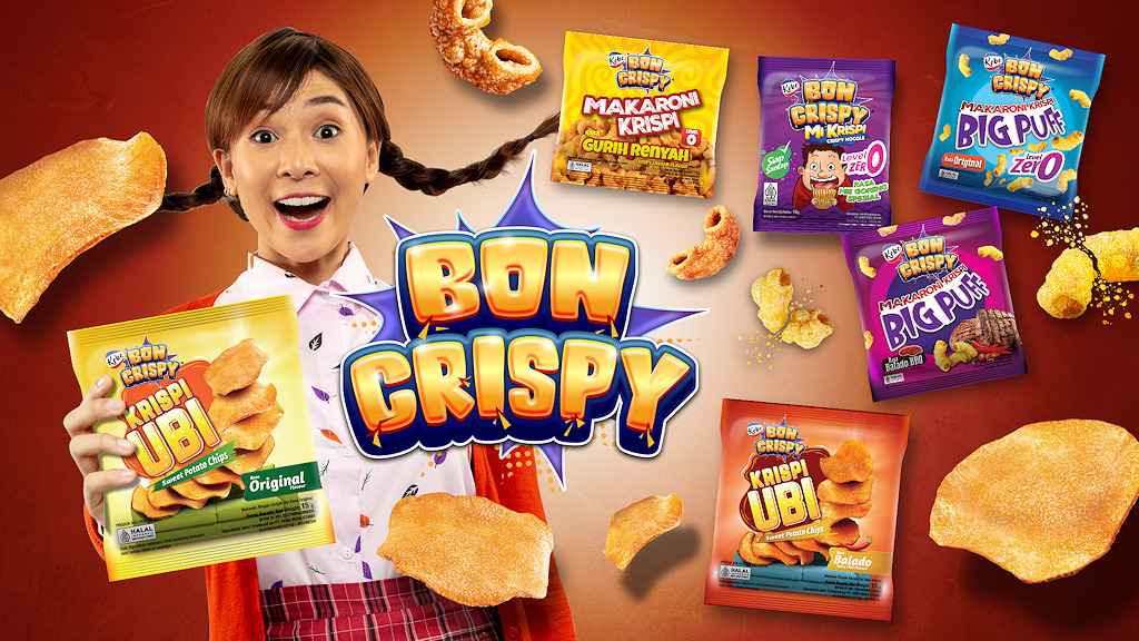 Seorang perempuan tersenyum memegang Bon Crispy Kripsi Ubi Original, dikelilingi logo Bon Crispy, berbagai kemasan makaroni, mi krispi, Big Puff, keripik ubi, dan potongan camilan di latar merah-oranye.
